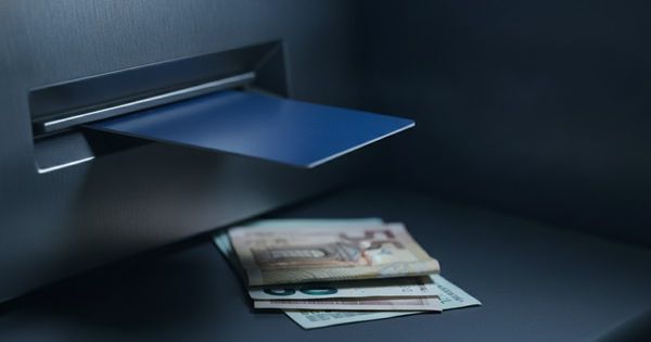 Macro studio shot of a credit card entering an ATM slot with cash bills fanned beside it