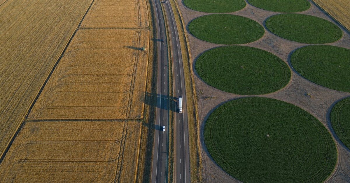 Aerial drone view of a highway crossing between two differently colored farm landscapes